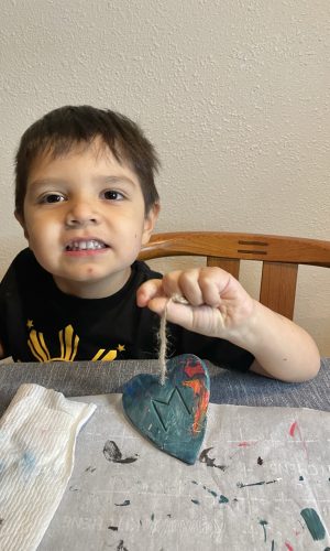 Boy smiling, holding painted heart clay sculpture