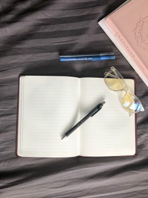 Journal laying flat with pen and glasses on top. Second pen & journal above.